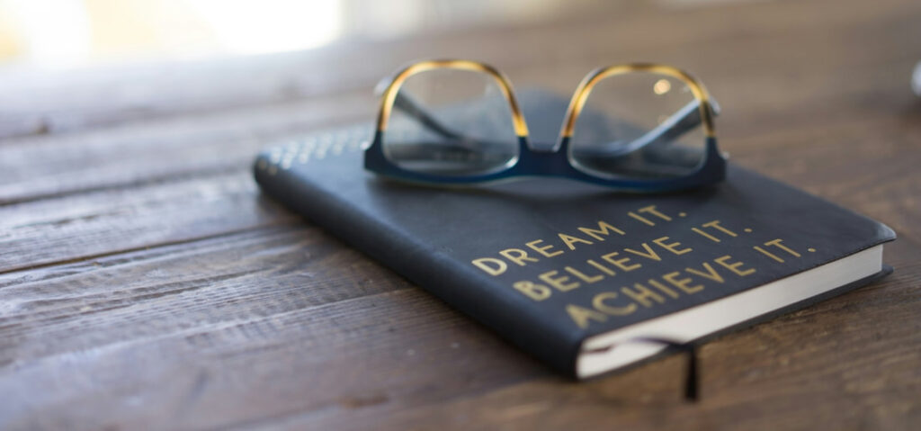 Dream it, believe it, achieve it - embossed book on table with a pair of glasses