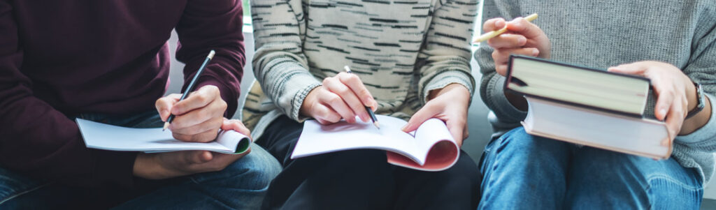 A group of three people with notebooks open on their laps and pens poised over the paper
