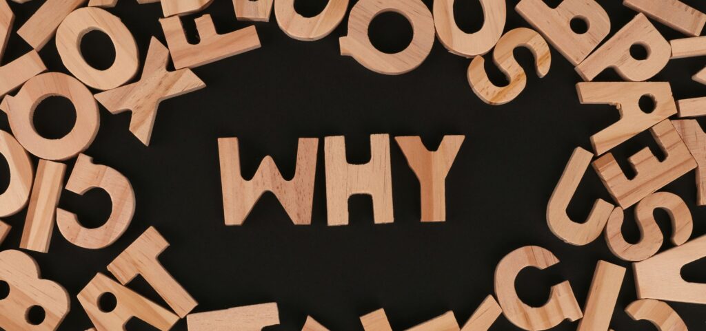 Jumbled wooden letters against a black background spelling out the word WHY