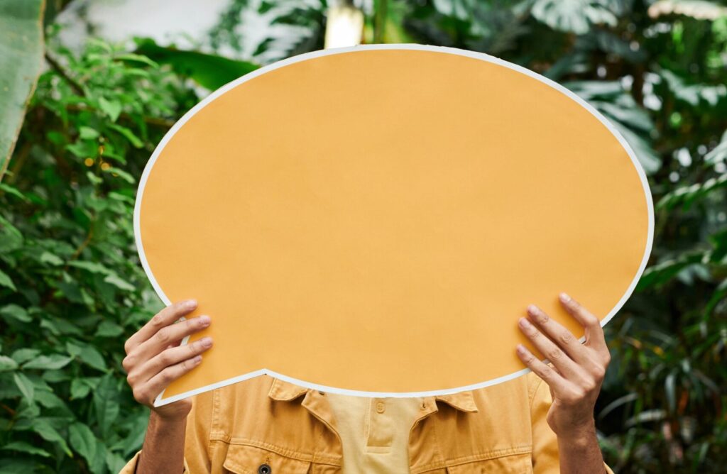 person holding up an orange dialogue bubble in a natural setting