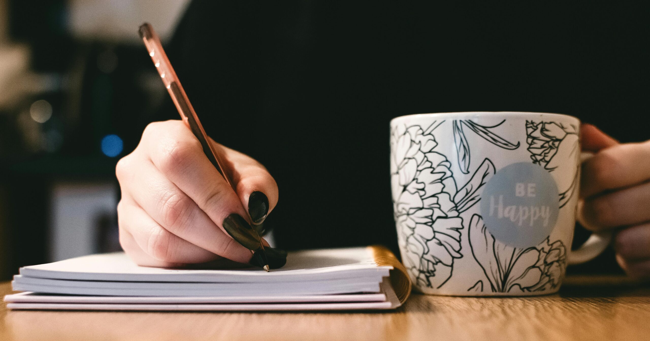 Author writes at a table with a mug that reads BE HAPPY