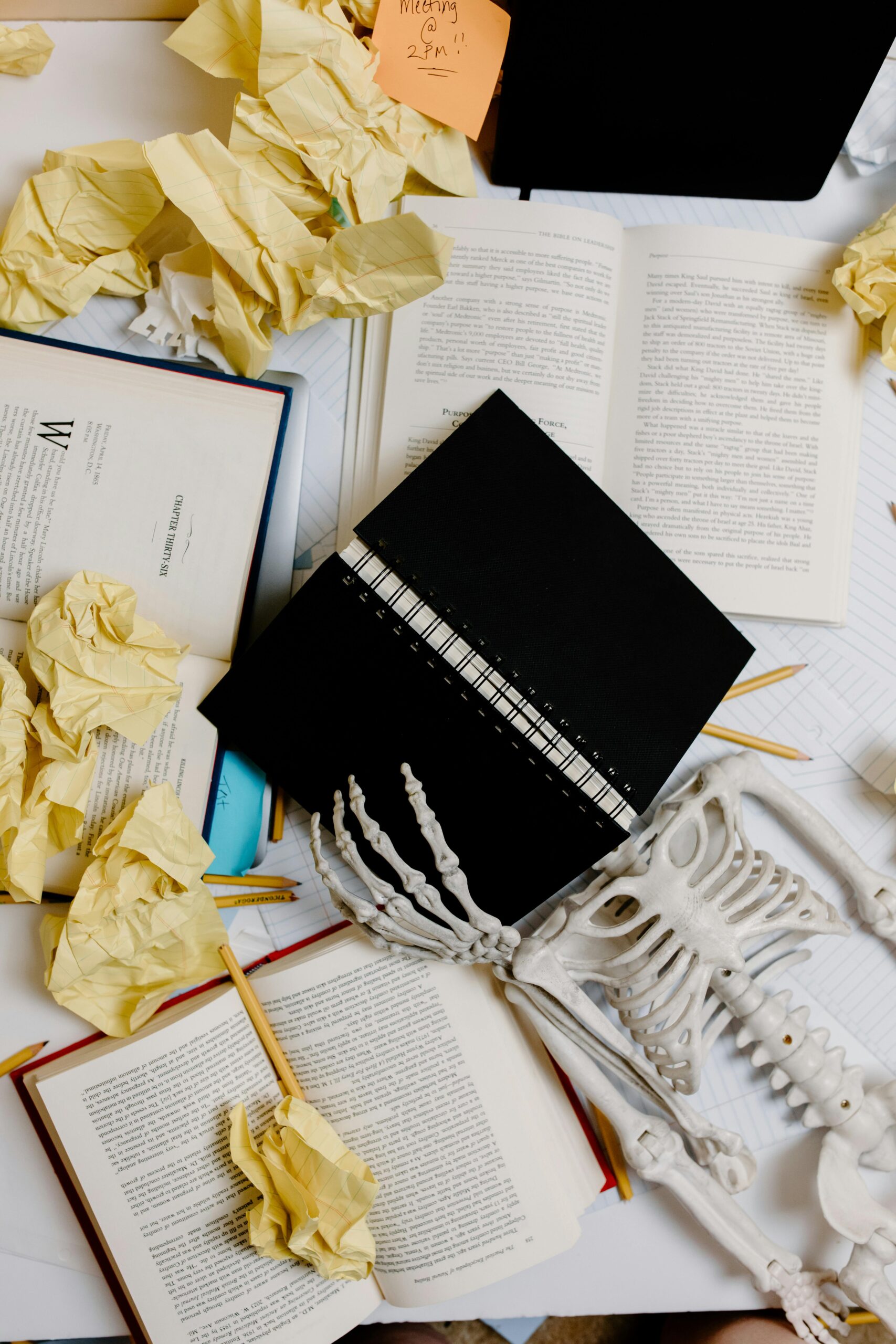 A skeleton amidst books and crumpled paper symbolizing academic burnout.