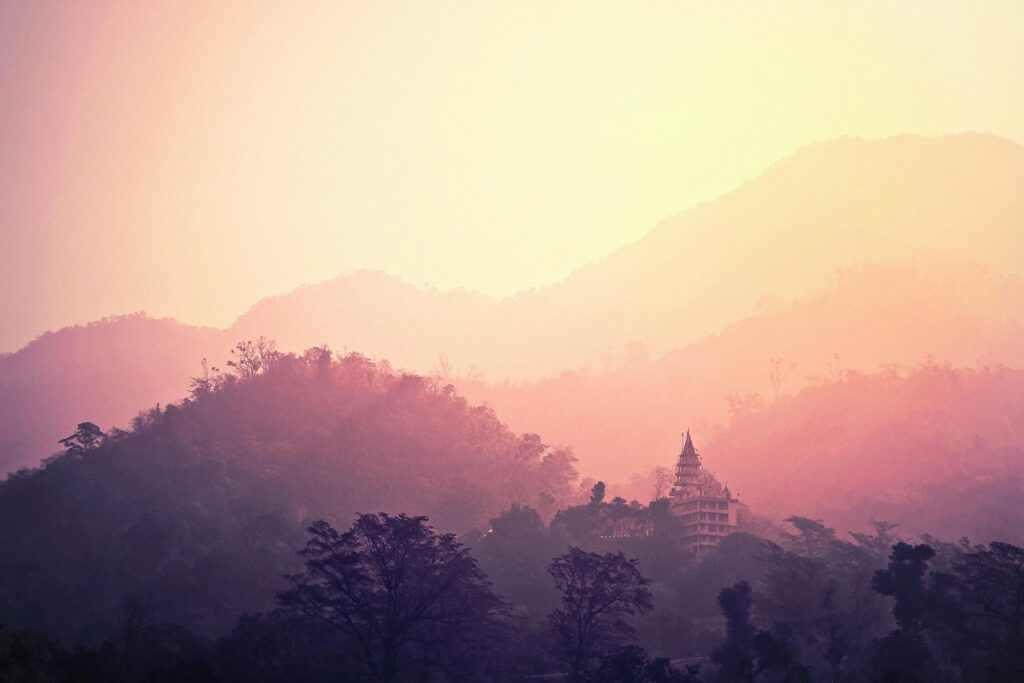 A tranquil view of Rishikesh mountains and temple enveloped in pink hues at sunrise.