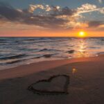 Beautiful sunset over ocean with a heart shape in the sand, perfect for romantic themes.