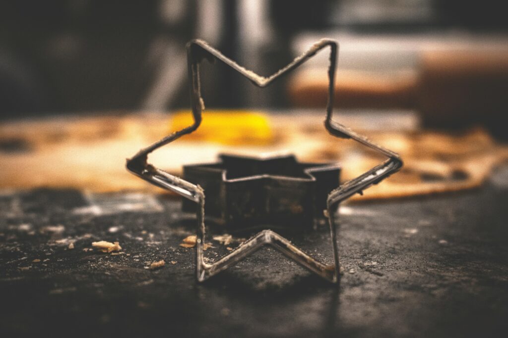 Close-up of a vintage star-shaped metal cookie cutter on a rustic table, with blurred baking background. Represents the role of setting in shaping the atmosphere of a work of fiction.