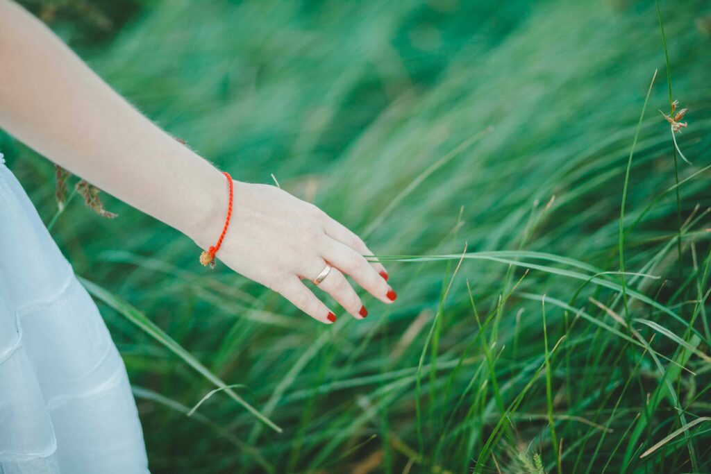 A woman's hand with red nails and bracelet gently touches lush green grass outdoors. Represents the use of sensory detail as one means by which authors can create mood through settings.