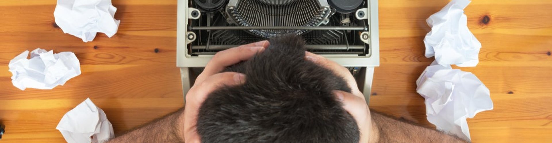 Writer at typewriter with head in hands surrounded by crumpled pages